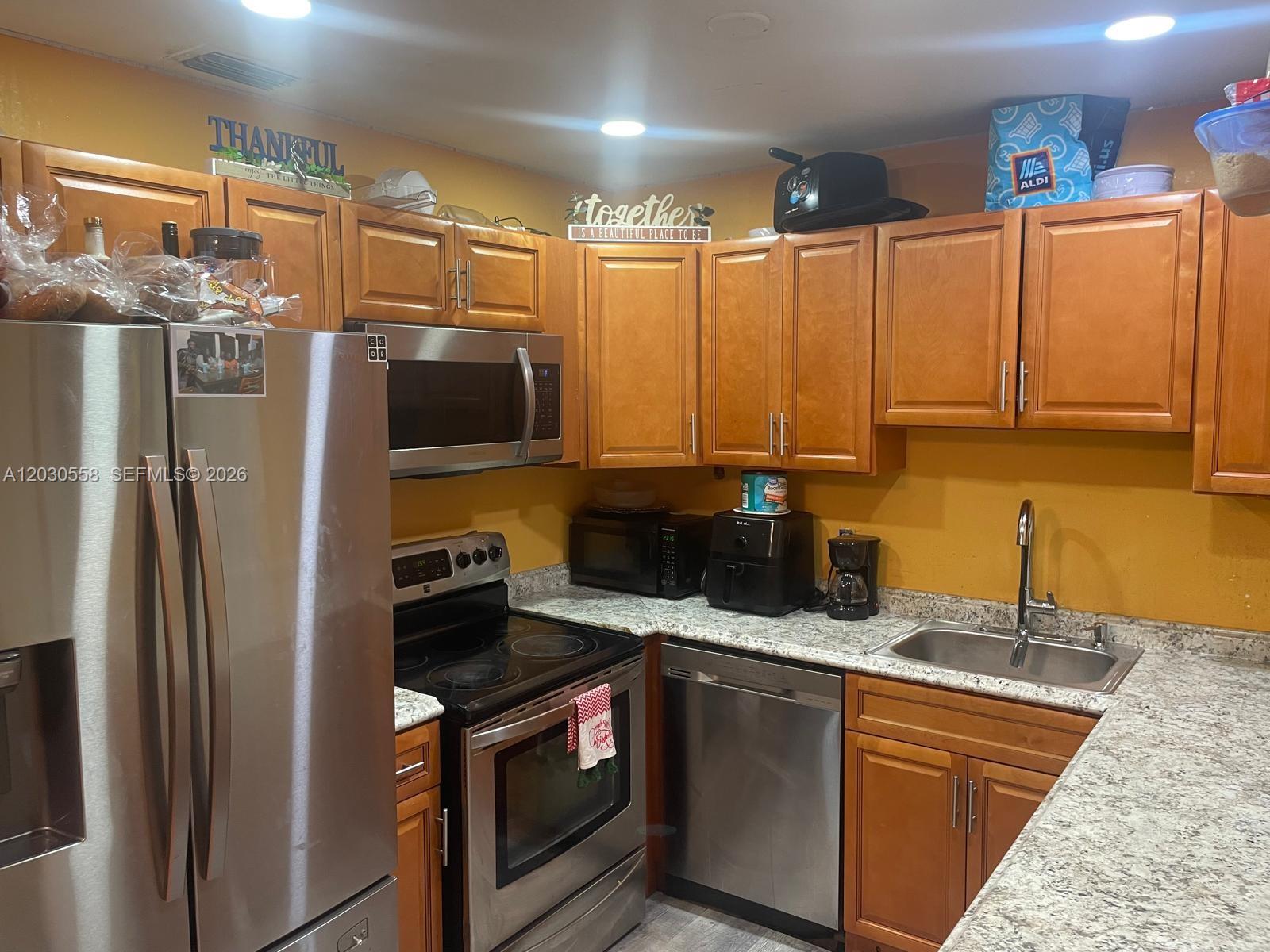 A kitchen features wood cabinets, stainless steel appliances, and granite countertops against yellow walls — 691 NW 20th Ct, Pompano Beach FL 33060, POMPANO BEACH, FL
