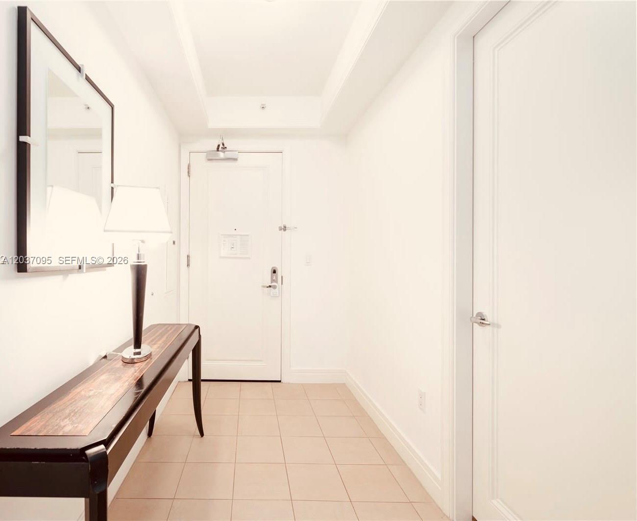 A hallway features white walls, tile flooring, a console table with a lamp, and doors — 1435 Brickell Ave # 3412, Miami FL 33131, MIAMI, FL
