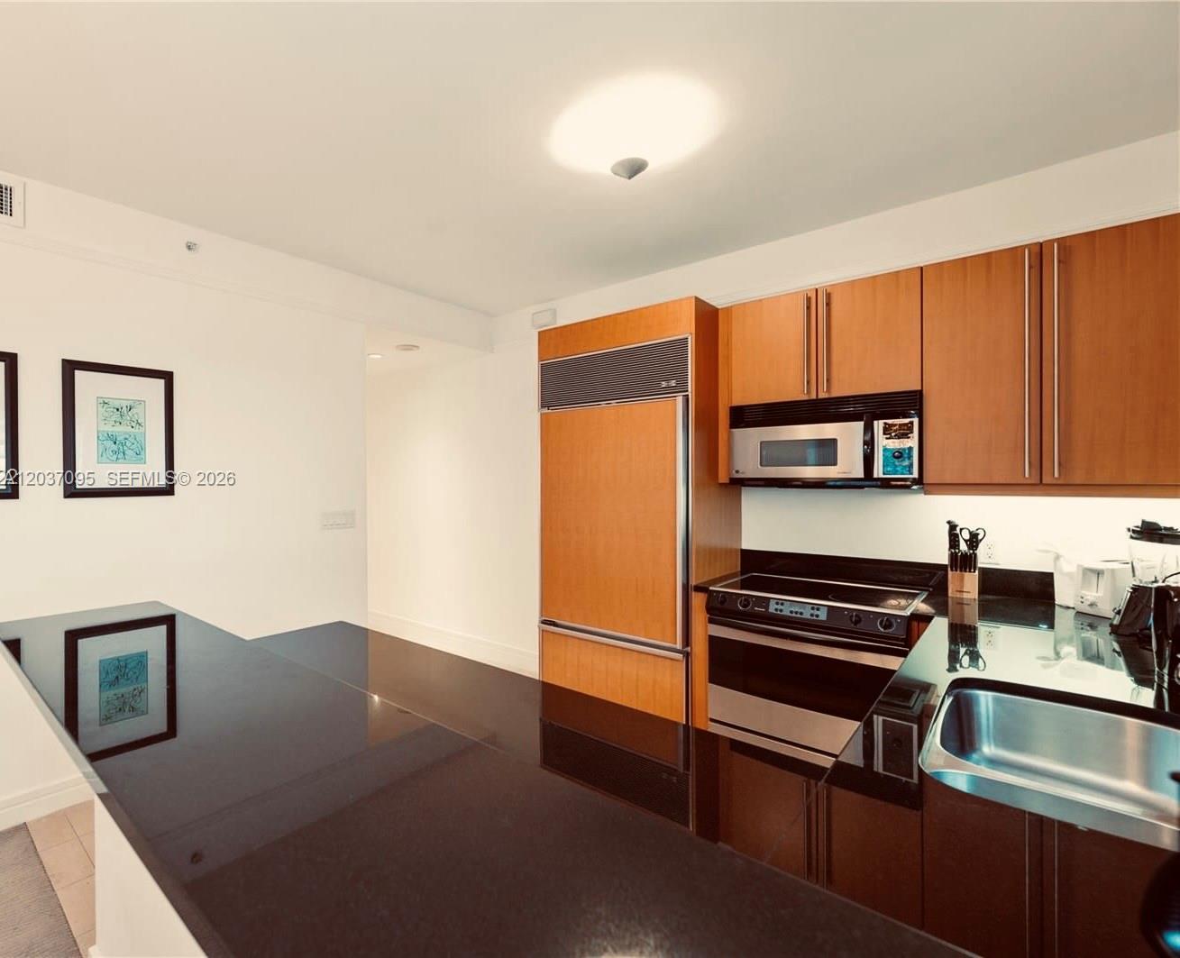 A kitchen features wood cabinetry, stainless steel appliances, and a black countertop island — 1435 Brickell Ave # 3412, Miami FL 33131, MIAMI, FL