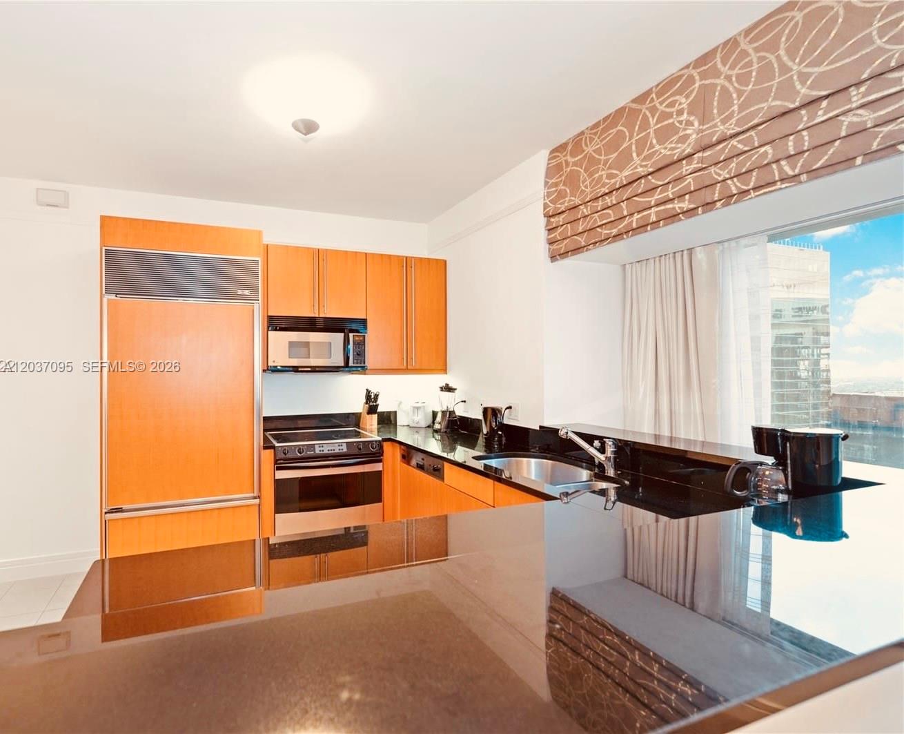 A kitchen features light wood cabinets, black countertops, stainless steel appliances, and a window view — 1435 Brickell Ave # 3412, Miami FL 33131, MIAMI, FL