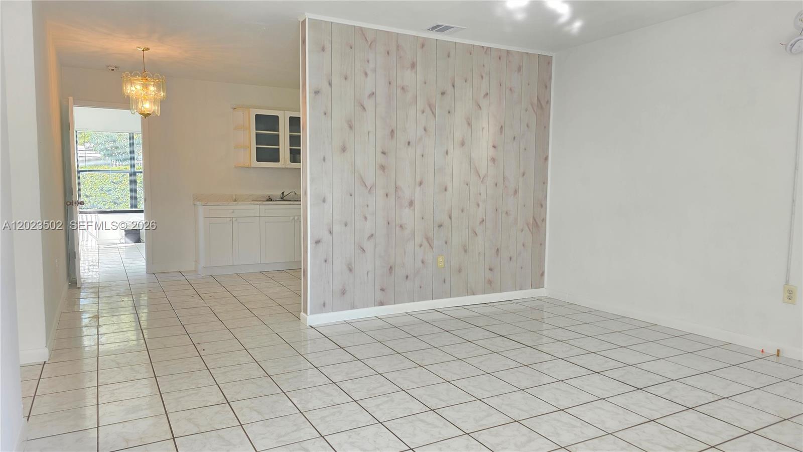 A room with white tile floors features a wood-paneled accent wall and an adjacent kitchen — 525 NE 132nd Ter, North Miami FL 33161, NORTH MIAMI, FL
