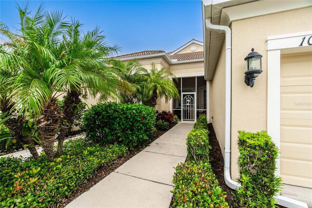 A concrete walkway leads to a screened front entryway beside a tan house exterior — 10924 LERWICK CIRCLE, ENGLEWOOD, FL