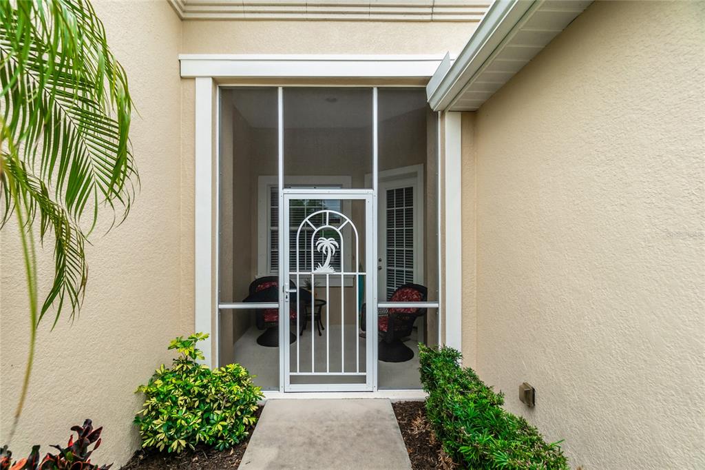 A white metal screen door with a palm tree design leads into a covered entryway — 10924 LERWICK CIRCLE, ENGLEWOOD, FL
