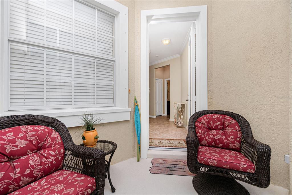 A covered patio features two wicker chairs with red floral cushions and a small table — 10924 LERWICK CIRCLE, ENGLEWOOD, FL
