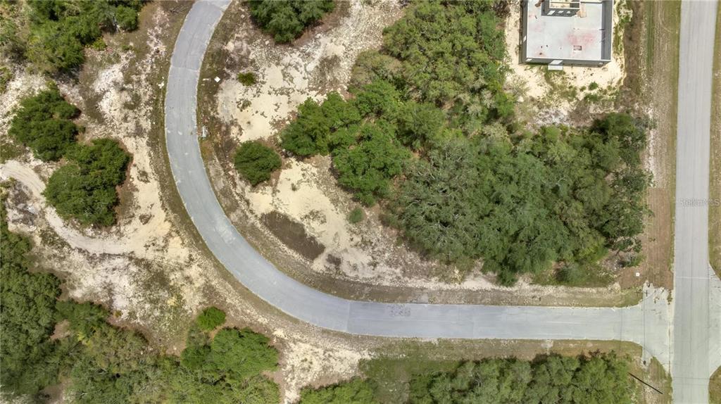 An aerial view shows a curved paved road winding through a wooded, undeveloped residential lot — 1418 SARASOTA COURT, KISSIMMEE, FL