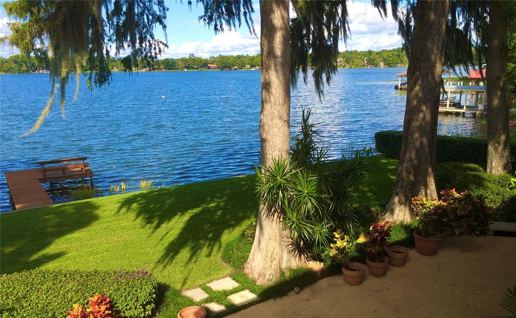 A grassy backyard leads to a wooden dock on a lake with large shade trees — 2655 LAKE SHORE DRIVE, ORLANDO, FL