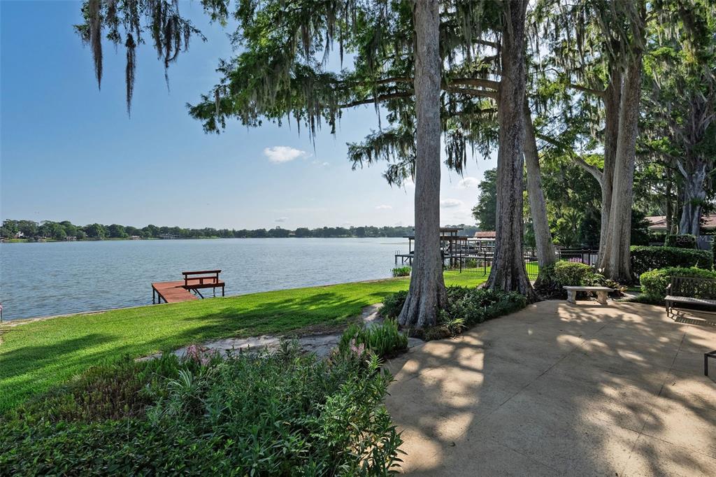 A grassy lawn leads to a lake with a wooden dock under large cypress trees — 2655 LAKE SHORE DRIVE, ORLANDO, FL