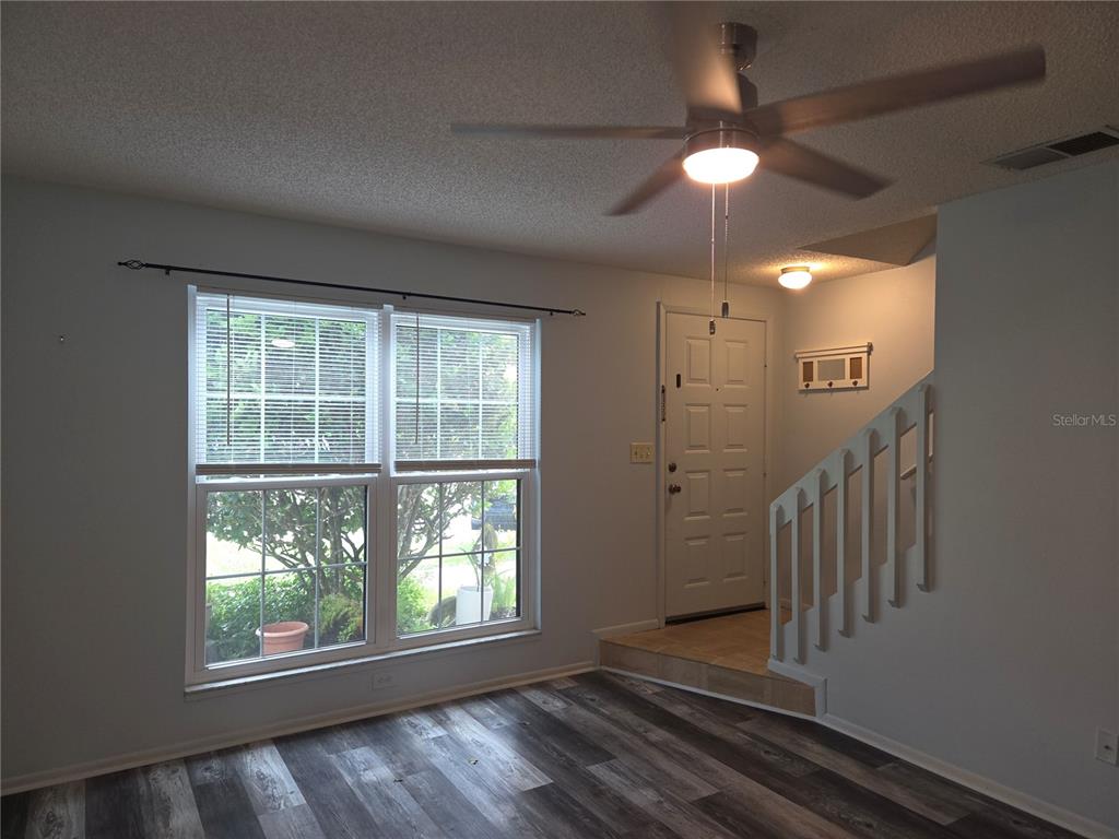 A living room with wood-look flooring, a ceiling fan, a window, and stairs to an entryway — 1701 SE 24TH ROAD UNIT 103, OCALA, FL