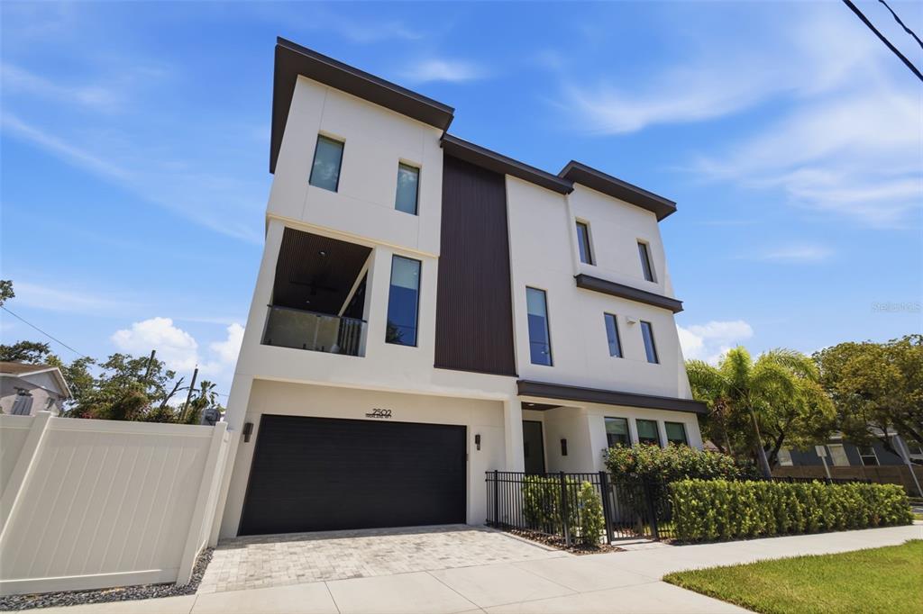 A modern three-story house features a black garage door, white stucco walls, and dark accents — 2502 N HIGHLAND AVENUE UNIT 1, TAMPA, FL