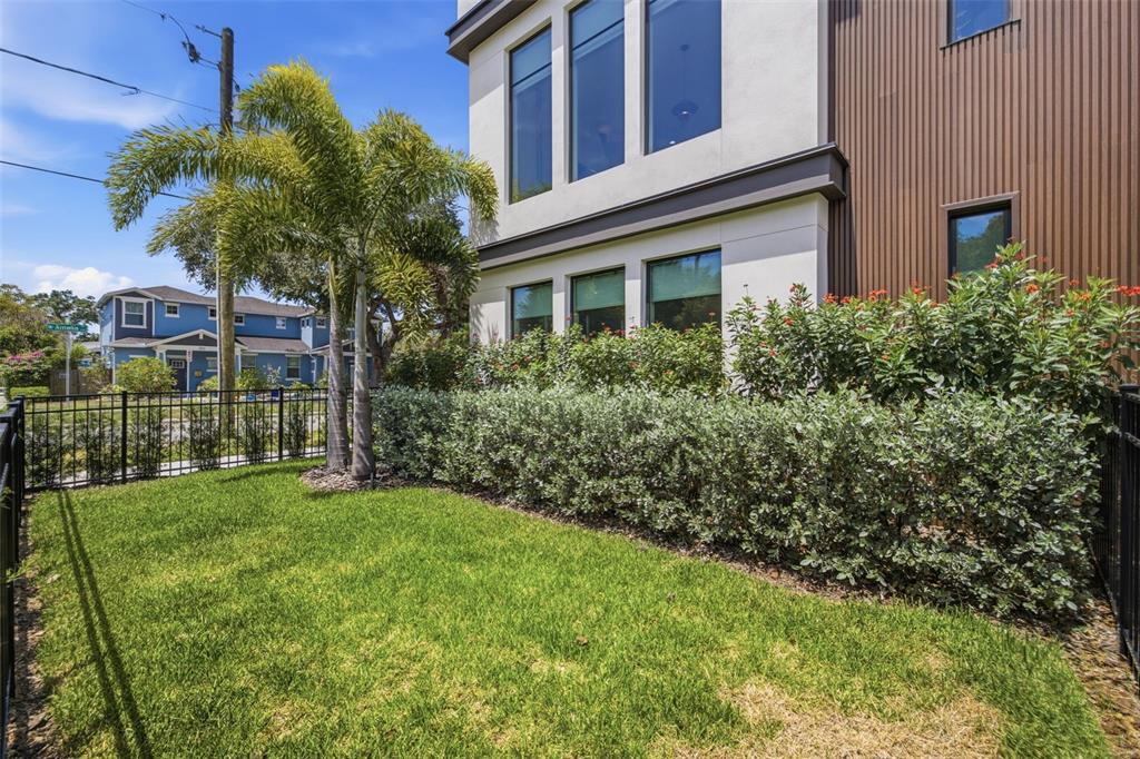 A small grassy yard with a palm tree sits beside a modern multi-story home — 2502 N HIGHLAND AVENUE UNIT 1, TAMPA, FL