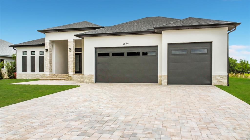 A modern single-story house with a stone-accented facade, a three-car garage, and a paved driveway — 9524 SINGER CIRCLE, PORT CHARLOTTE, FL
