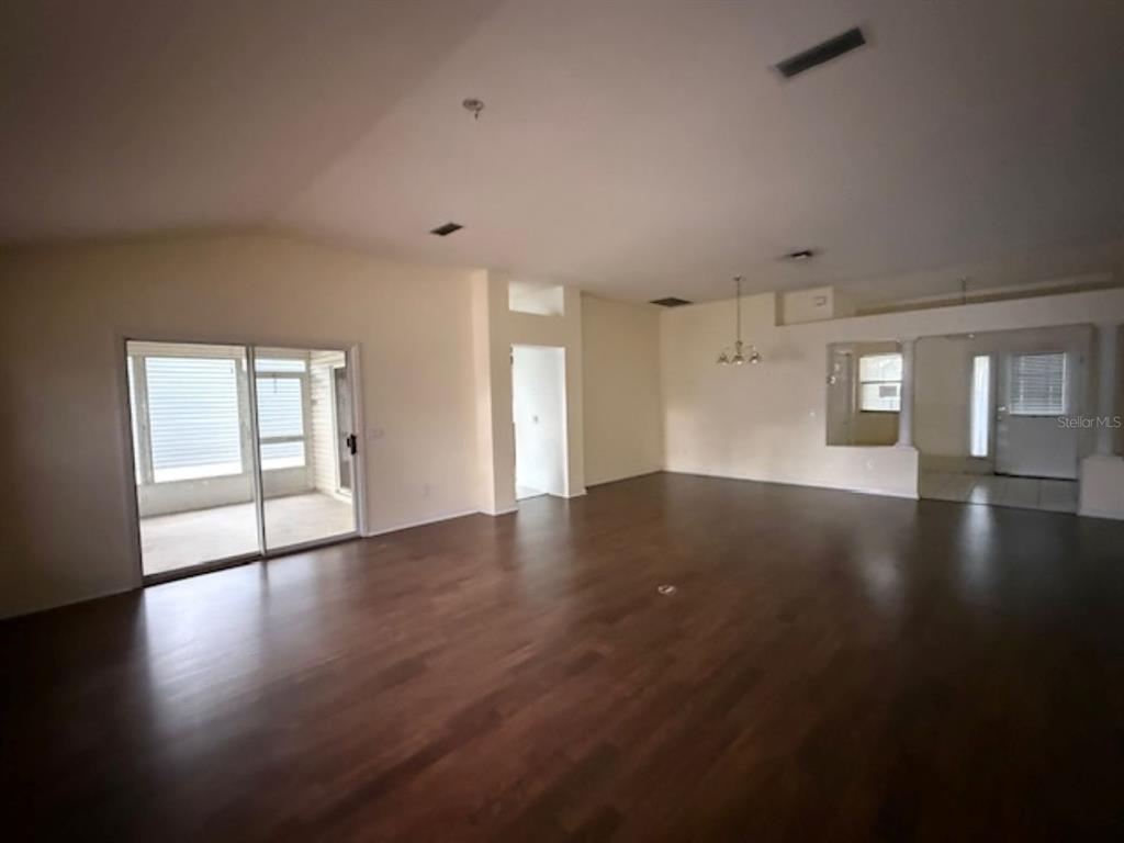 A spacious living area features dark wood flooring, a vaulted ceiling, and sliding glass doors — 1109 MONTEREY LANE, LADY LAKE, FL
