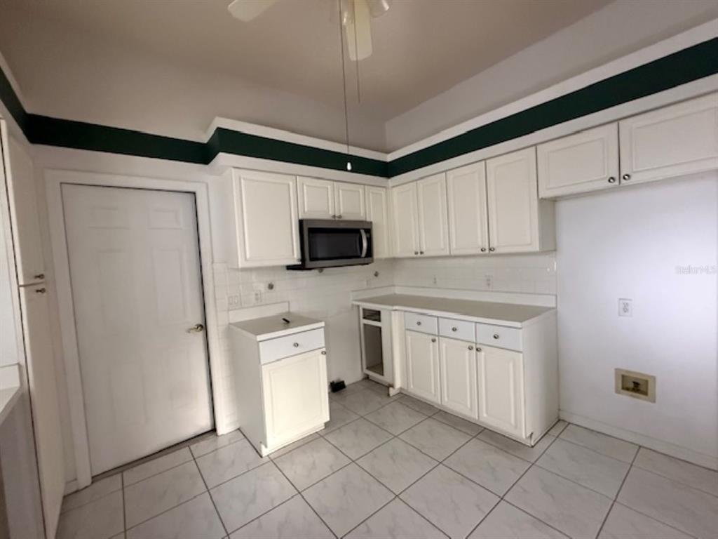 A kitchen with white cabinets, a microwave, tiled floors, and a dark green wall border — 1109 MONTEREY LANE, LADY LAKE, FL