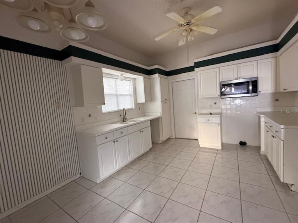 A kitchen with white cabinets, tile flooring, a ceiling fan, and a striped accent wall — 1109 MONTEREY LANE, LADY LAKE, FL
