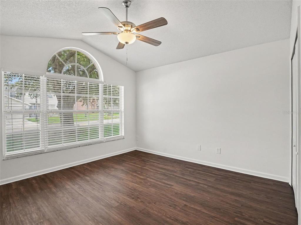 An empty bedroom features white walls, dark wood-look flooring, a ceiling fan, and arched windows — 15854 BAY VISTA DRIVE, CLERMONT, FL