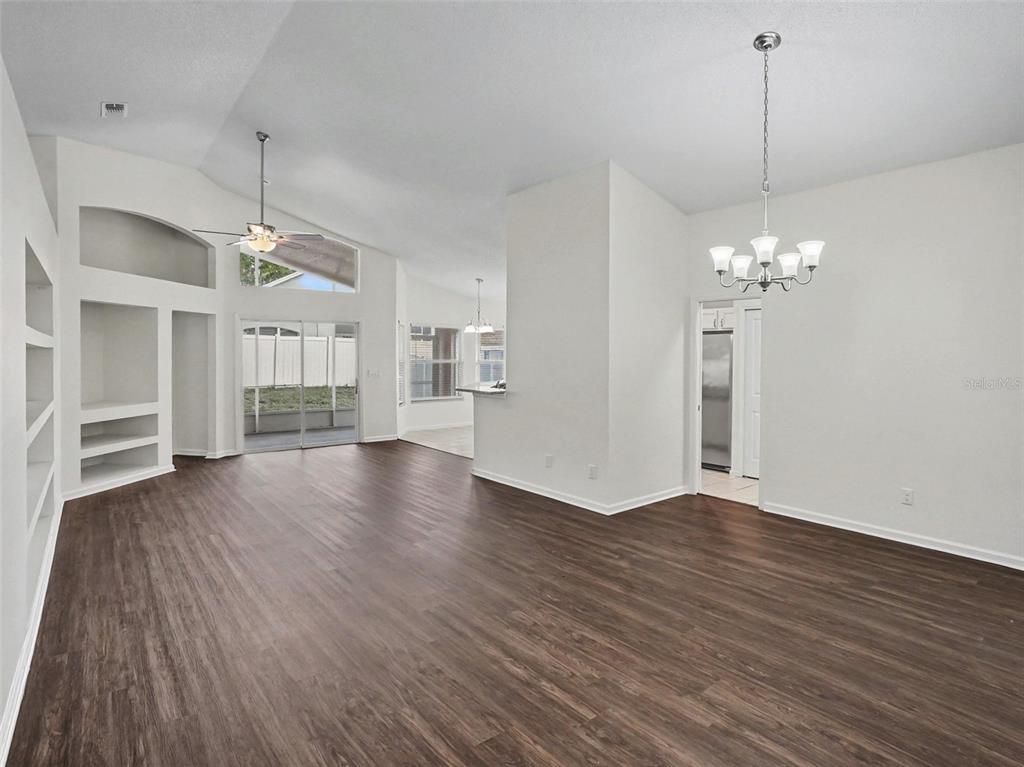 An open-concept living area features dark wood-look flooring, vaulted ceilings, and a built-in shelving unit — 15854 BAY VISTA DRIVE, CLERMONT, FL