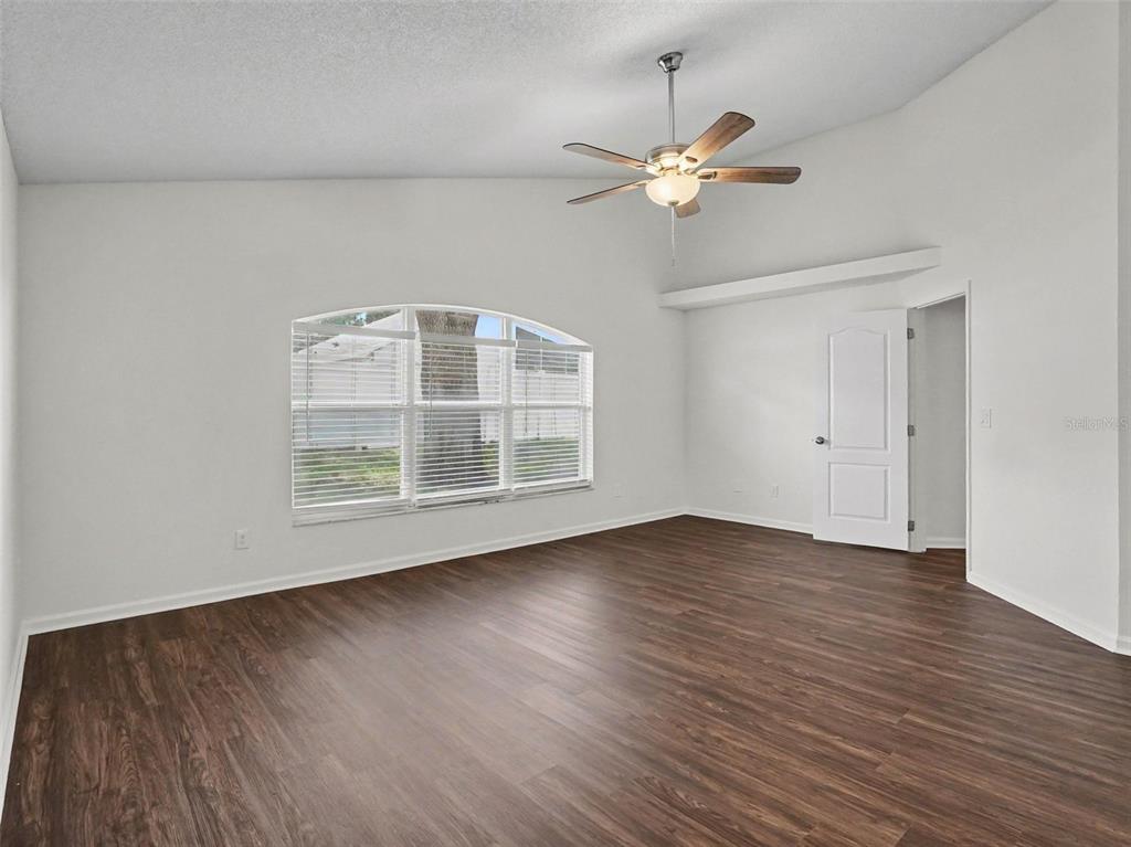 A spacious room with white walls, dark wood-look flooring, a ceiling fan, and arched window — 15854 BAY VISTA DRIVE, CLERMONT, FL