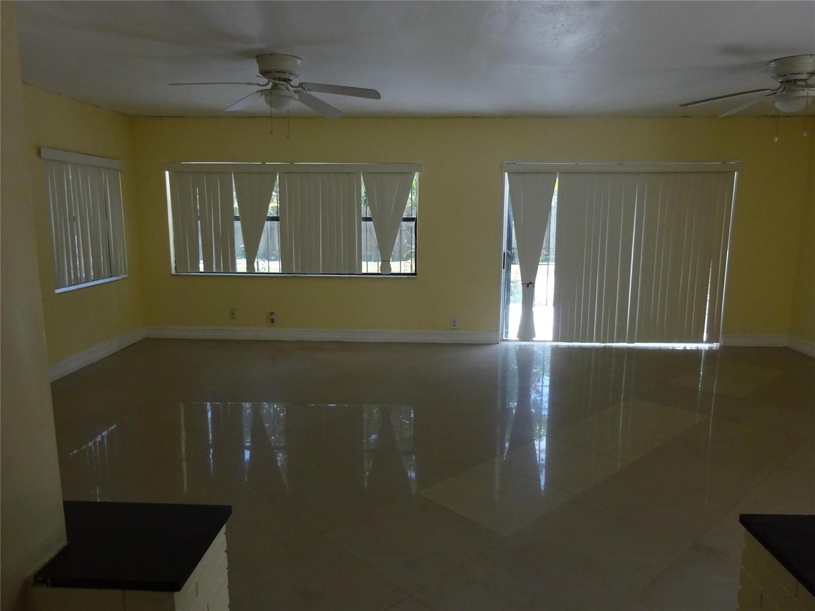 An empty room features yellow walls, large windows with vertical blinds, and glossy tile flooring — 740 E Evanston Circle E, Fort Lauderdale FL 33312, FORT LAUDERDALE, FL
