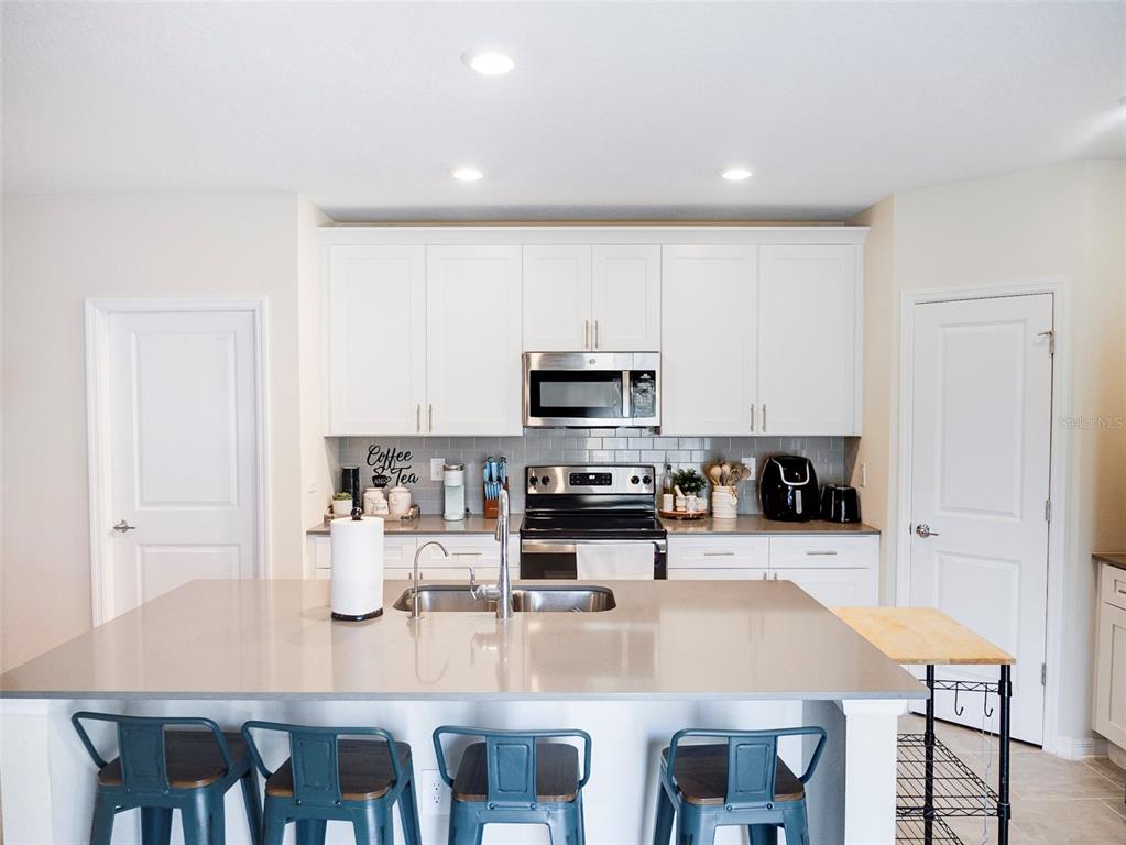 A kitchen features white cabinets, a gray island with bar seating, and stainless steel appliances — 2949 MULLER OAK LOOP, OCOEE, FL
