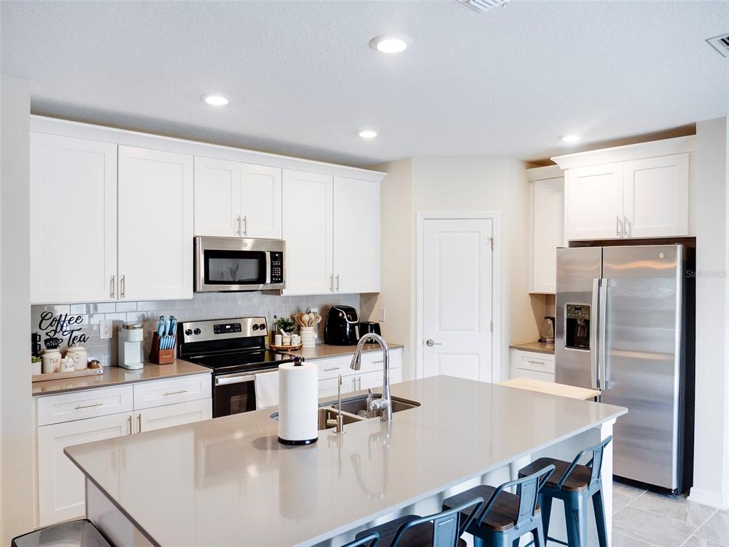 A modern kitchen features white cabinets, stainless steel appliances, and a large gray island — 2949 MULLER OAK LOOP, OCOEE, FL