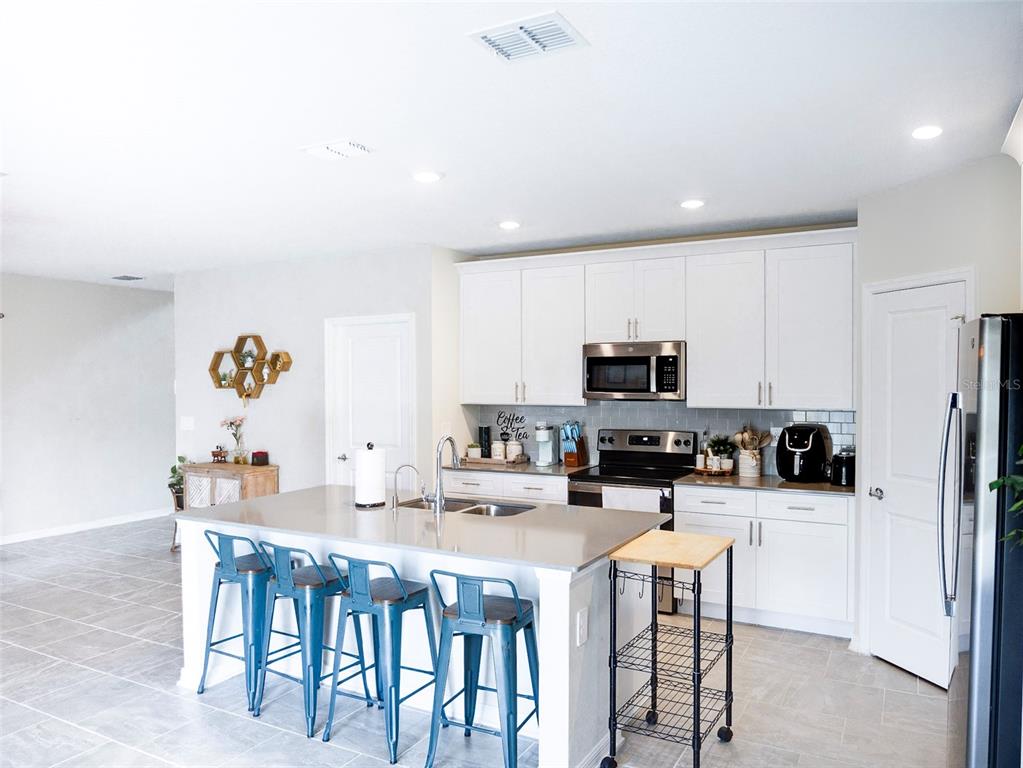 A kitchen features white cabinets, a gray island with blue stools, and stainless steel appliances — 2949 MULLER OAK LOOP, OCOEE, FL