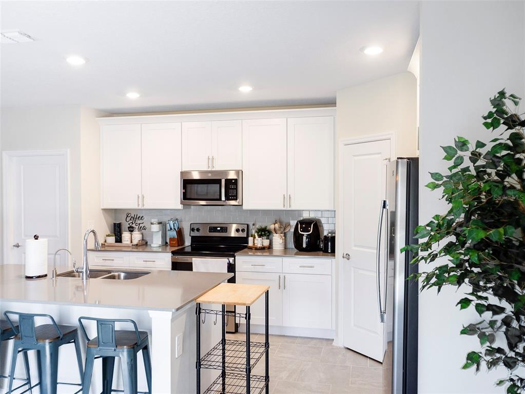 A kitchen features white cabinets, stainless steel appliances, a gray island, and tile flooring — 2949 MULLER OAK LOOP, OCOEE, FL