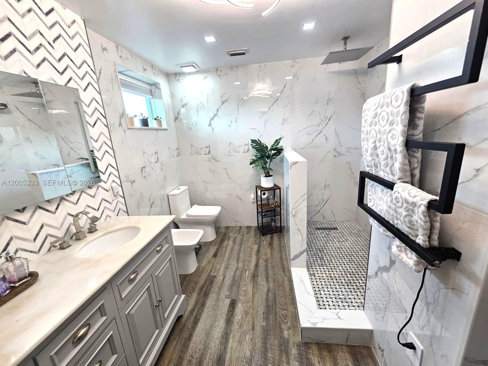 A modern bathroom features a marble-tiled shower, a grey vanity, and wood-look flooring — 15429 SW 92nd St, Miami FL 33196, MIAMI, FL