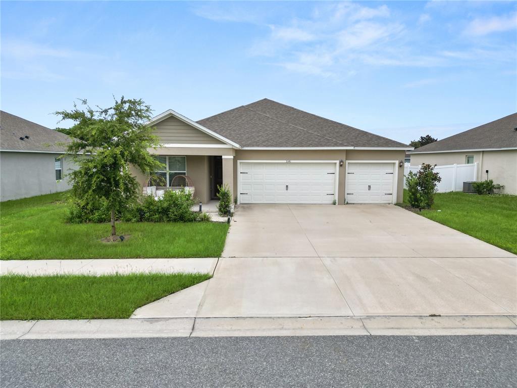 A single-story house with a tan exterior, a three-car garage, and a front lawn — 3141 CASPIAN FEATHER STREET, BARTOW, FL