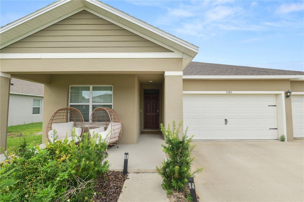The exterior of a single-story house features a covered porch, two wicker chairs, and a garage — 3141 CASPIAN FEATHER STREET, BARTOW, FL