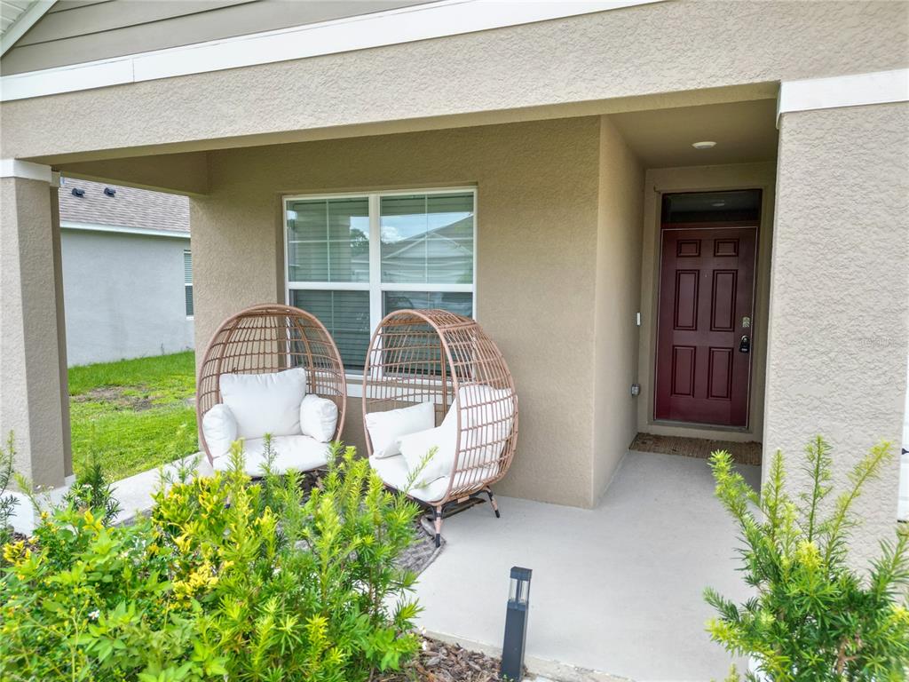 A covered front porch features two wicker egg chairs and a dark red front door — 3141 CASPIAN FEATHER STREET, BARTOW, FL