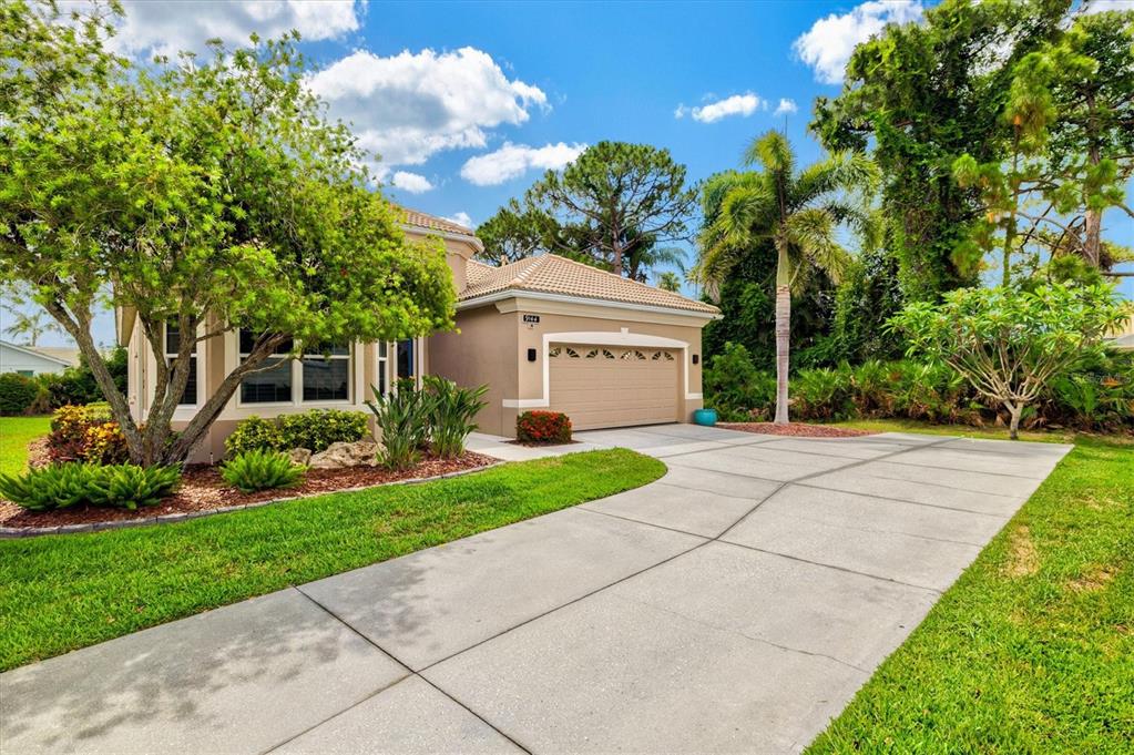 A single-story house with a tan stucco exterior, a tile roof, and a concrete driveway — 9144 WILLOW BROOK DRIVE, SARASOTA, FL