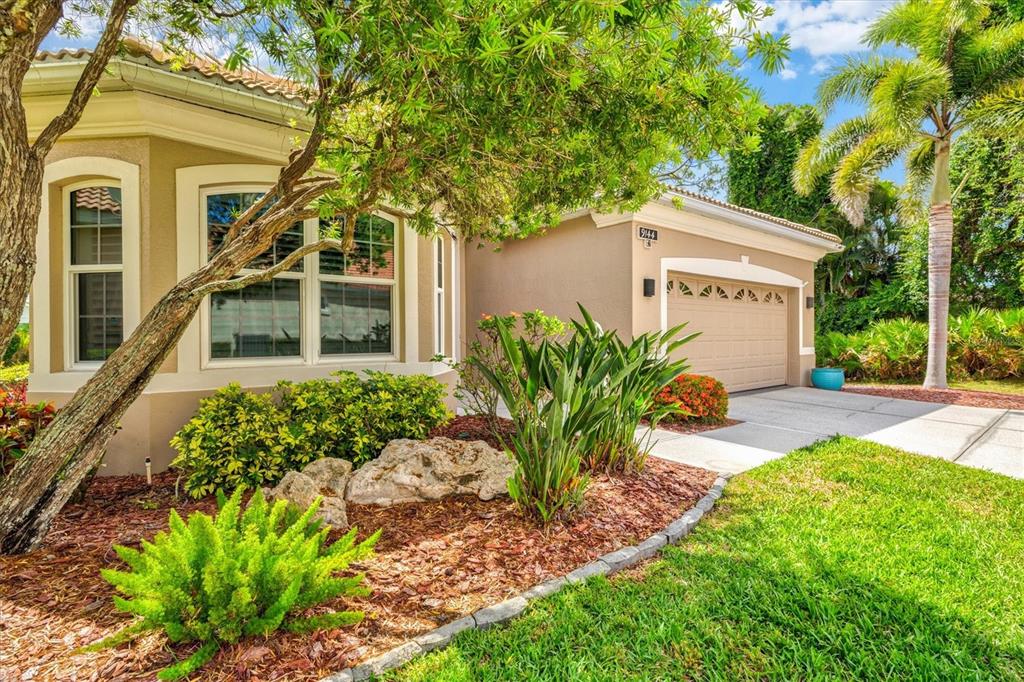 The exterior of a tan house features a garage, a bay window, and landscaped front yard — 9144 WILLOW BROOK DRIVE, SARASOTA, FL