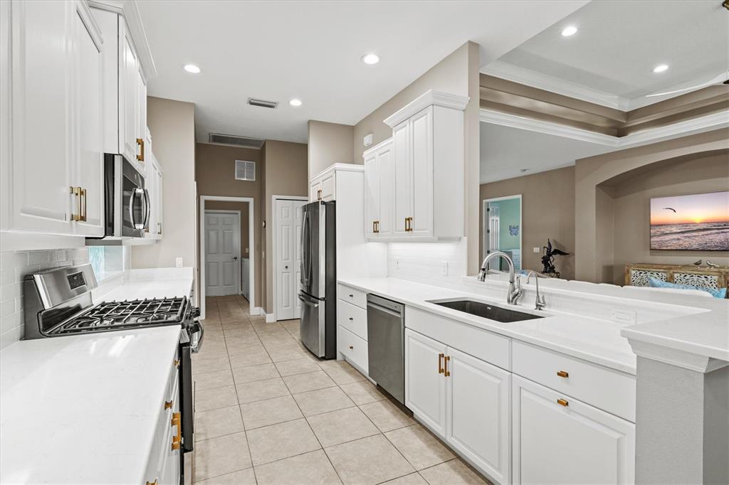 A bright kitchen features white cabinets, stainless steel appliances, and a pass-through sink counter — 9144 WILLOW BROOK DRIVE, SARASOTA, FL