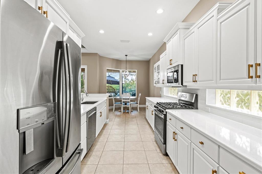 A kitchen features white cabinets, stainless steel appliances, quartz countertops, and a dining nook — 9144 WILLOW BROOK DRIVE, SARASOTA, FL