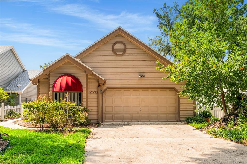 A tan, single-story house with a front-facing garage, a red awning, and a concrete driveway — 278 BLACKWATER PLACE, LONGWOOD, FL