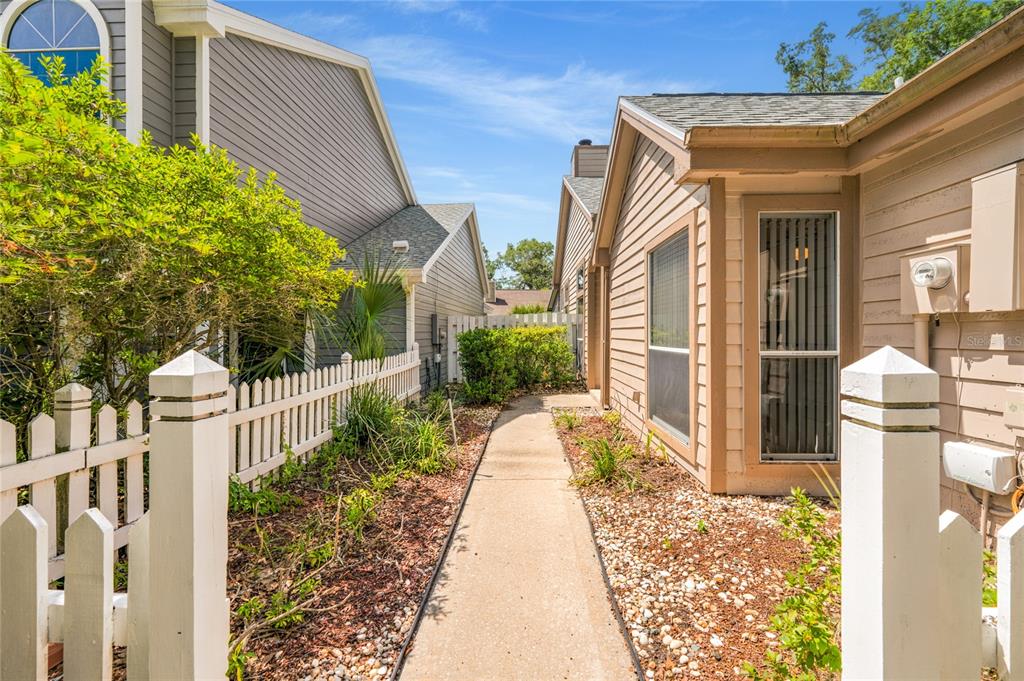 A concrete walkway leads between two residential buildings with light-colored siding and a white fence — 278 BLACKWATER PLACE, LONGWOOD, FL