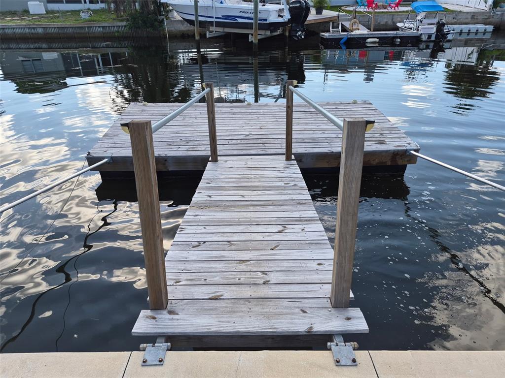 A wooden floating dock extends from a concrete bulkhead into a canal with boats — 13636 VERONICA DRIVE, HUDSON, FL