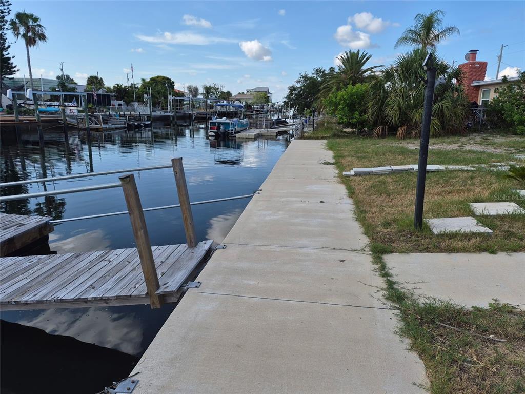 A concrete seawall borders a canal with a wooden dock and boats in the background — 13636 VERONICA DRIVE, HUDSON, FL