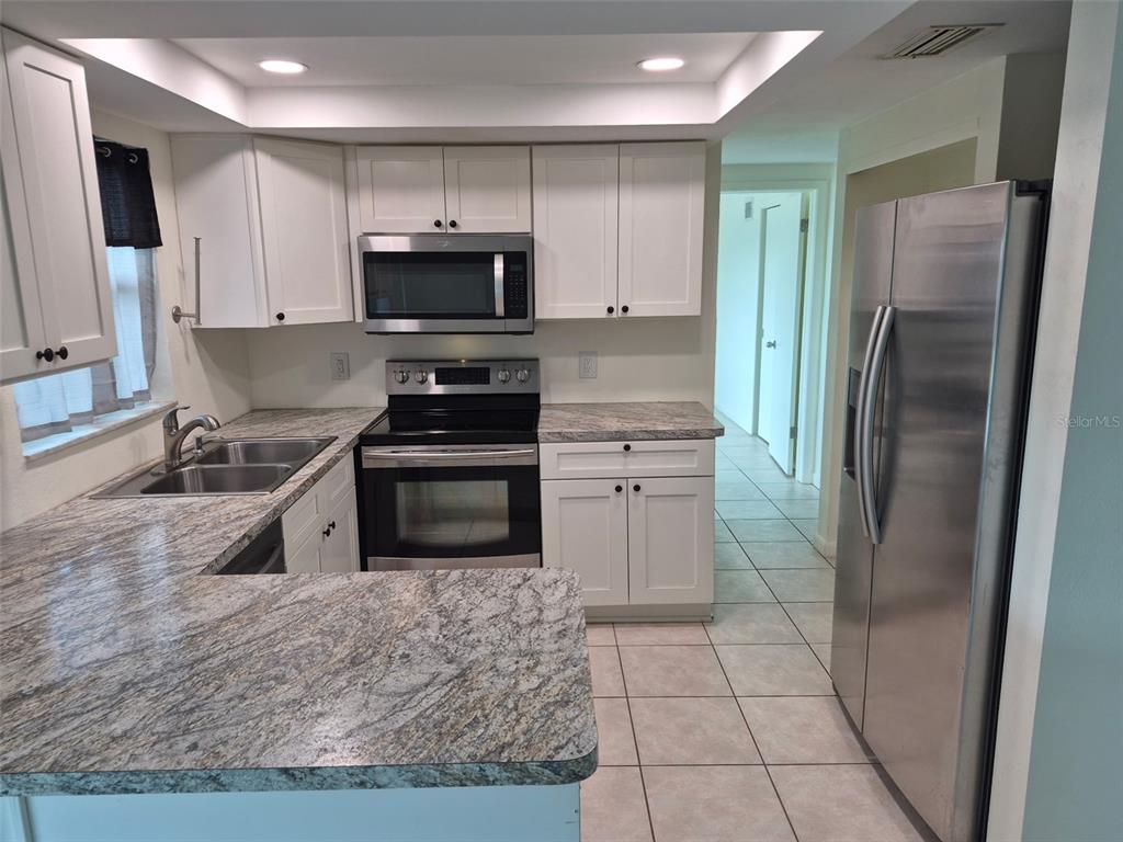 A kitchen features white cabinets, granite countertops, stainless steel appliances, and light-colored tile flooring — 13636 VERONICA DRIVE, HUDSON, FL