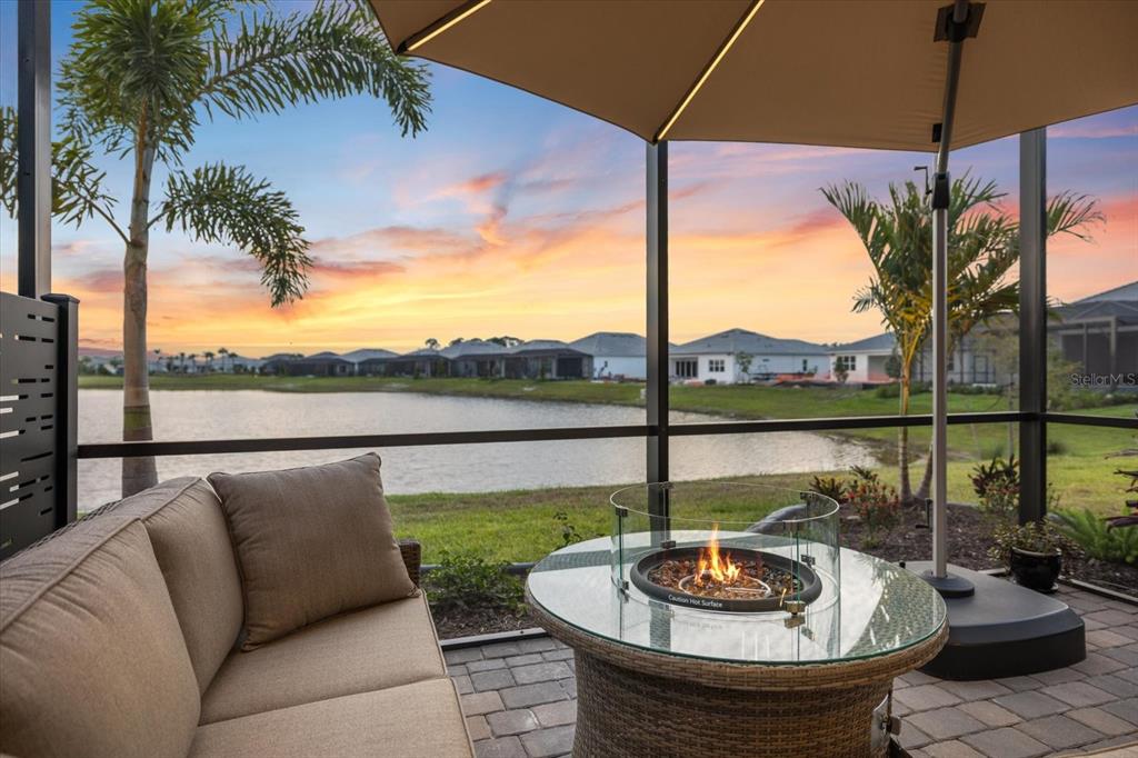 A screened-in patio features a wicker sofa, a glass-topped fire pit, and a lake view — 10333 BLUE RUNNER DRIVE, ENGLEWOOD, FL