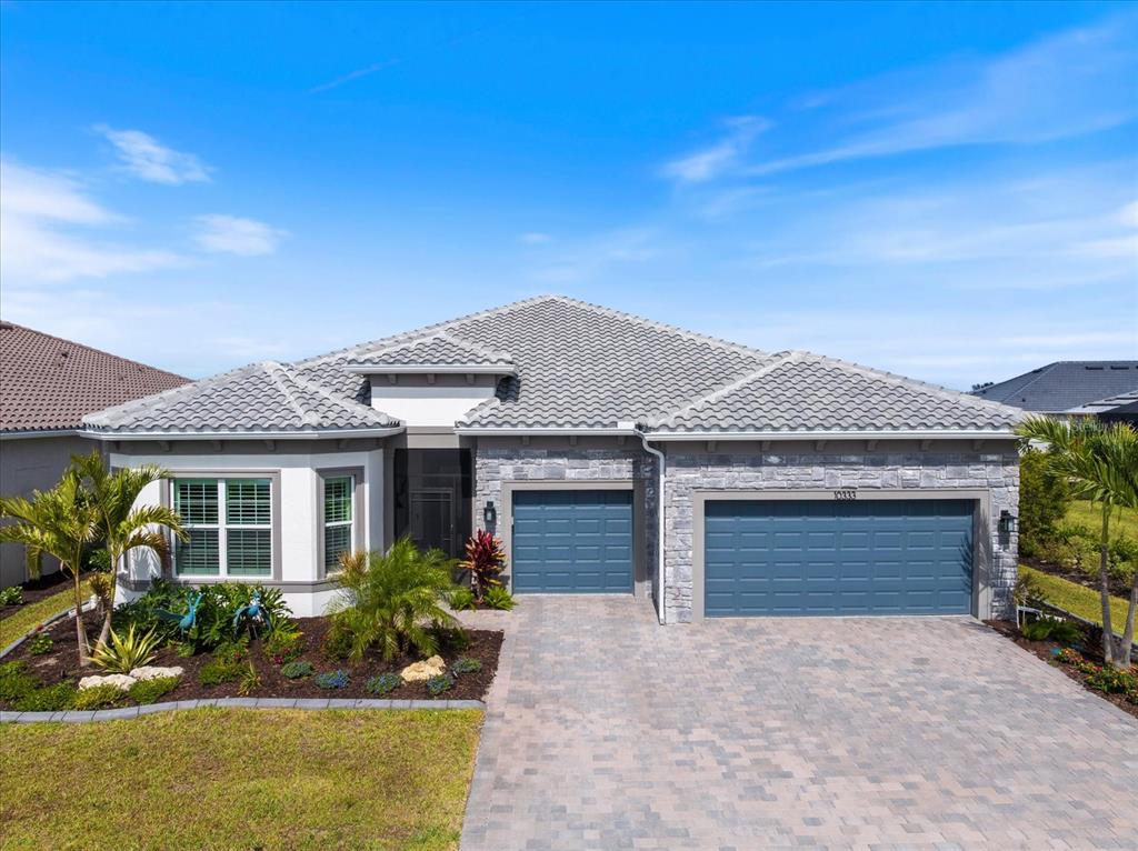 A single-story house features a gray tile roof, stone facade, and two blue garage doors — 10333 BLUE RUNNER DRIVE, ENGLEWOOD, FL