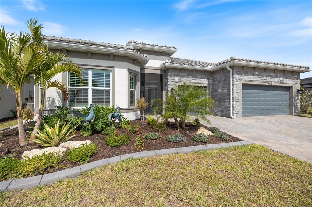 A single-story house with a stone facade, a gray garage door, and landscaped front yard — 10333 BLUE RUNNER DRIVE, ENGLEWOOD, FL