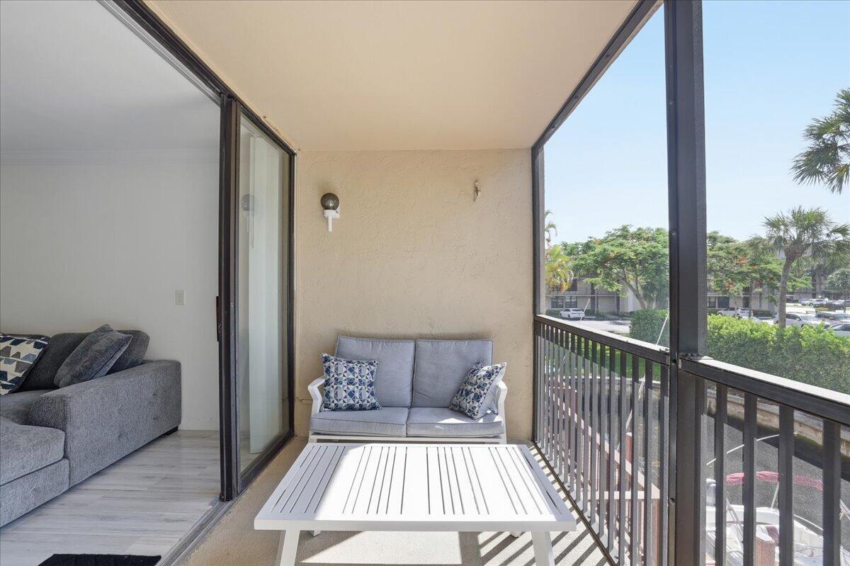 A screened-in balcony features a white coffee table, a light gray loveseat, and sliding doors — 16 Royal Palm Way # 205, Boca Raton FL 33432, BOCA RATON, FL