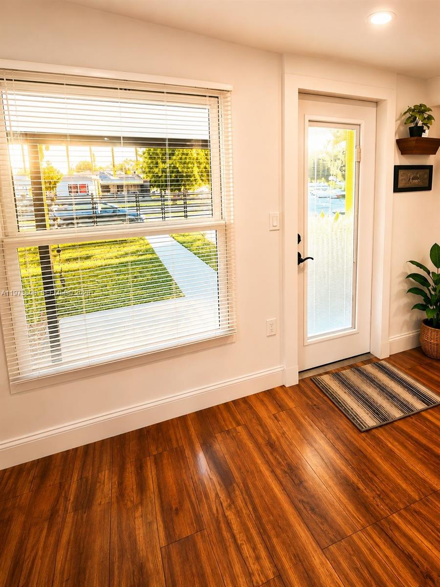 A room with wood-look flooring, a large window with blinds, and a glass-paneled exterior door — 2281 NW 81st Ter, Miami FL 33147, MIAMI, FL