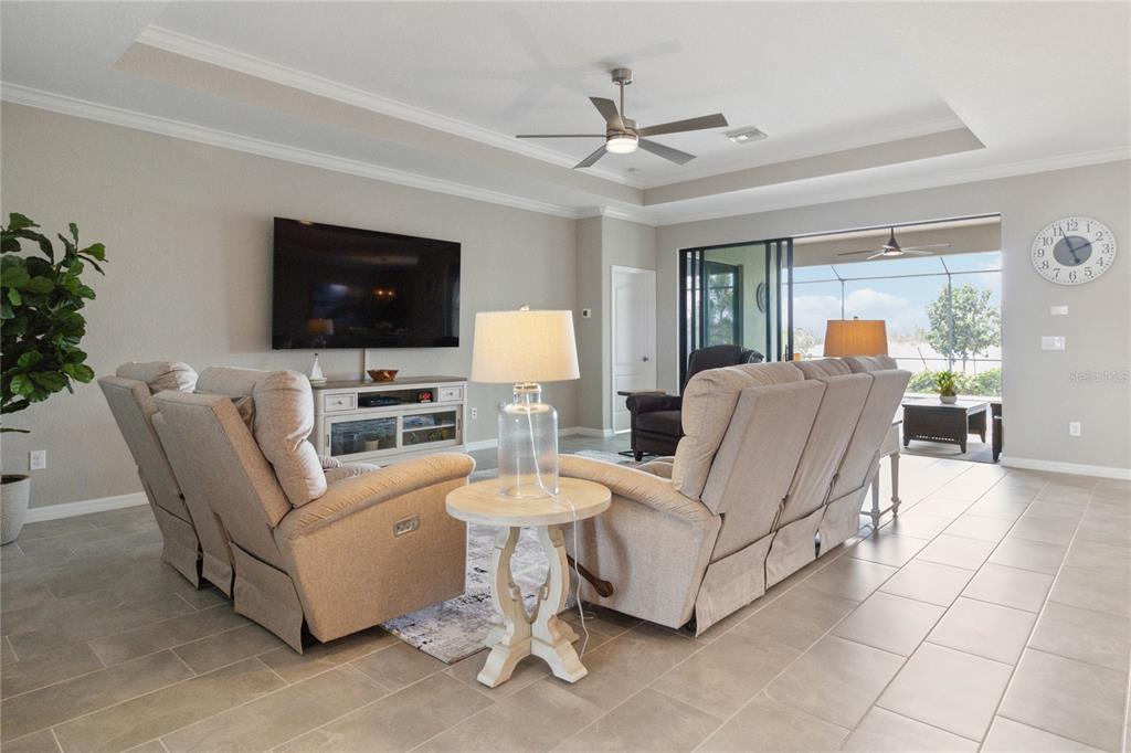 A living room features beige reclining sofas, a television, and a sliding door to a patio — 17724 POLO TRAIL, LAKEWOOD RANCH, FL