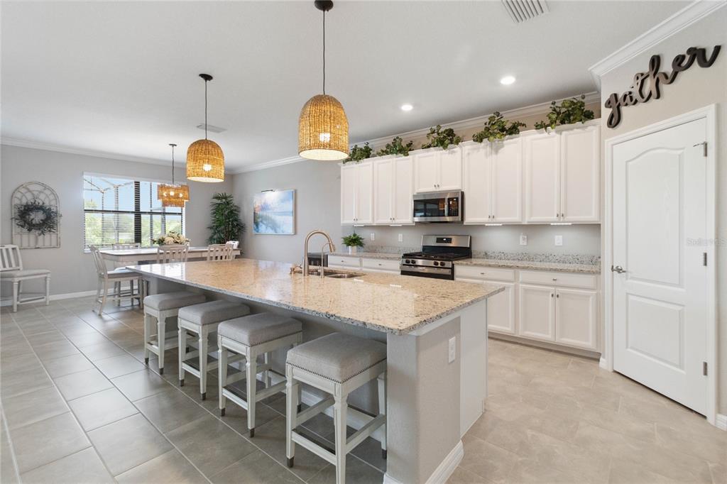 A kitchen features a large granite island with bar stools, white cabinetry, and pendant lighting — 17724 POLO TRAIL, LAKEWOOD RANCH, FL