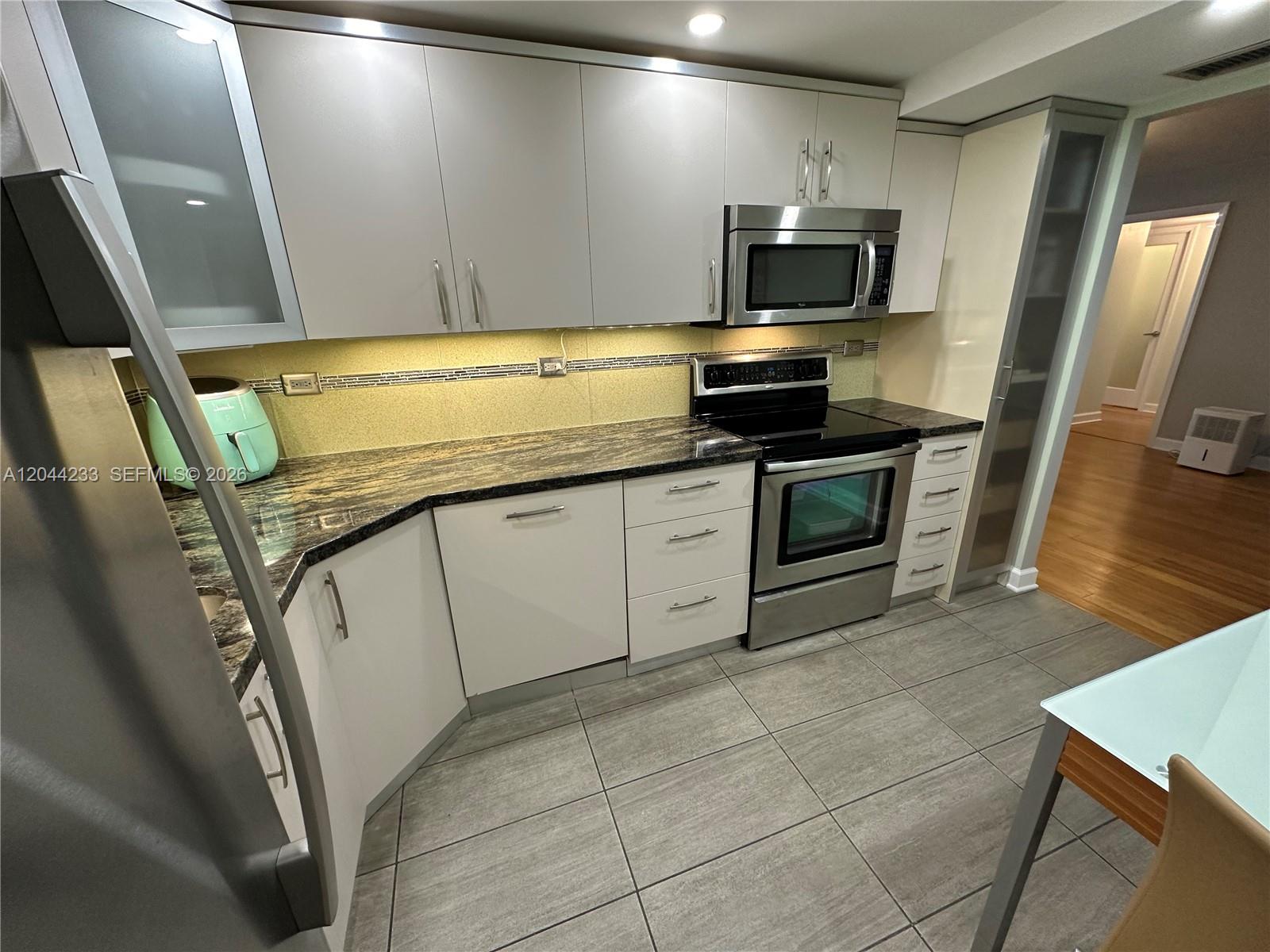 A kitchen features white flat-panel cabinets, dark granite countertops, stainless steel appliances, and tiled floors — 6039 Collins Ave # 1205, Miami Beach FL 33140, MIAMI BEACH, FL