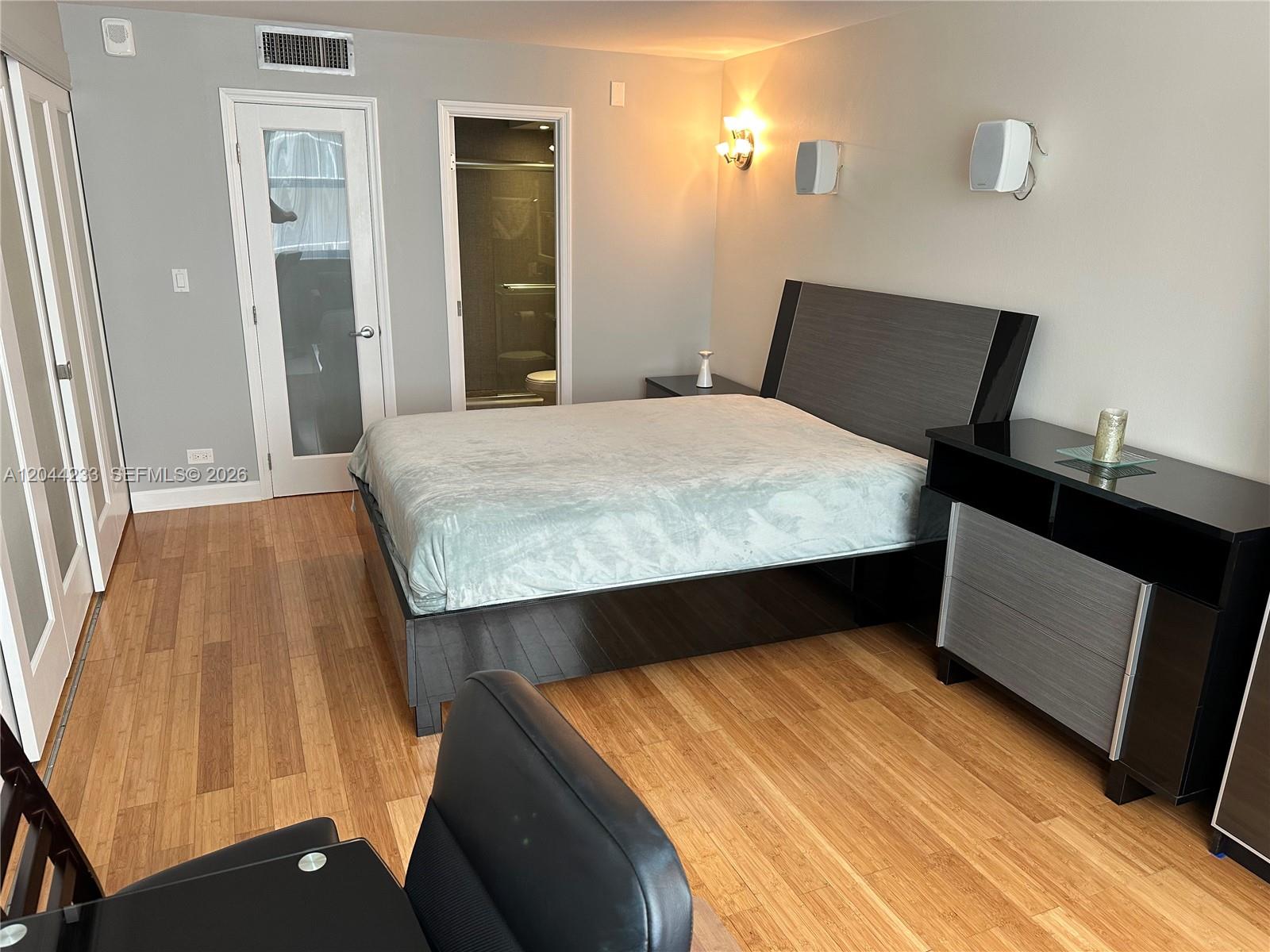 A bedroom features a bed, a dresser, wood flooring, and two doorways — 6039 Collins Ave # 1205, Miami Beach FL 33140, MIAMI BEACH, FL