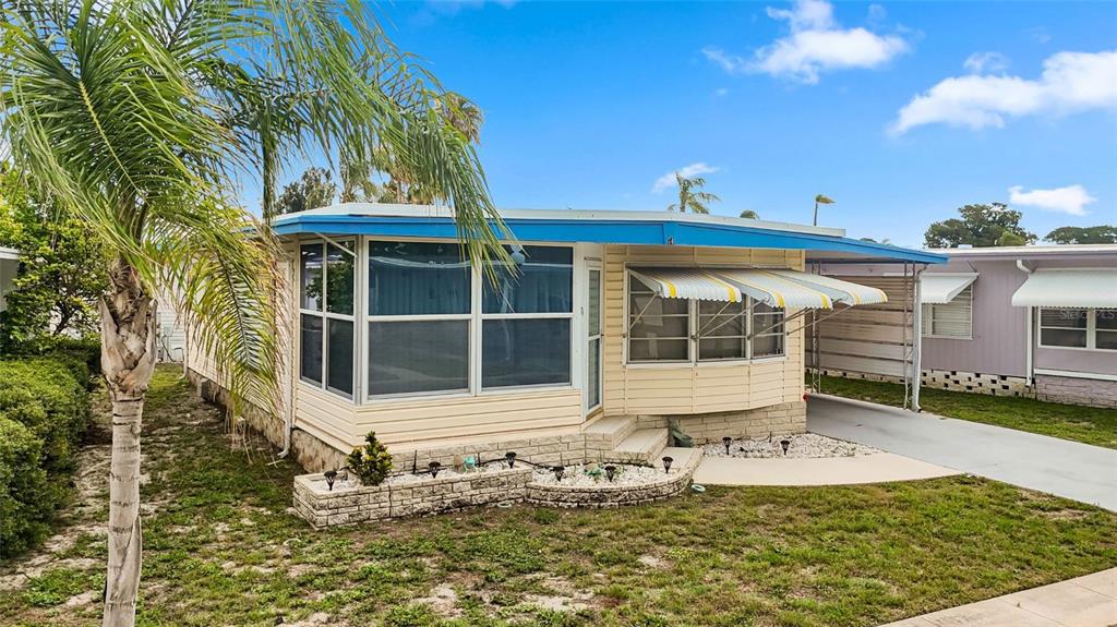 A single-story mobile home with light yellow siding, a blue roof, and a carport — 7901 40TH AVENUE N UNIT 74, ST PETERSBURG, FL