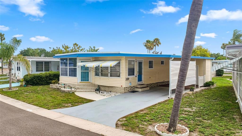 A light yellow mobile home features a blue trim, a carport, and a palm tree — 7901 40TH AVENUE N UNIT 74, ST PETERSBURG, FL